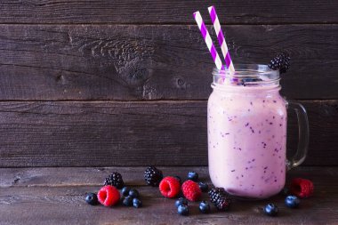 Karışık meyve püresi, mason kavanozu bardağında ve dağınık malzemelerle. Koyu ahşap zemin ile yan görünüm.