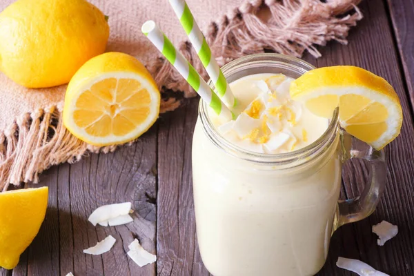 Kavanoz bardakta limonlu hindistan cevizli smoothie. Masa sahnesini koyu ahşap arka plana karşı kapat.
