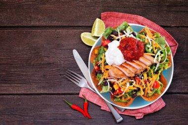 Chicken taco salad with sour cream and salsa. Mexican food dish. Above view table scene on a dark wood background. clipart