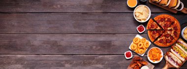 Abur cubur sınırı. Pizza, hamburger, tavuk kanadı, sosisli sandviç ve tuzlu atıştırmalıklar. Fotokopi alanı olan koyu ahşap bir arkaplan üzerine tepeden aşağı görünüm.