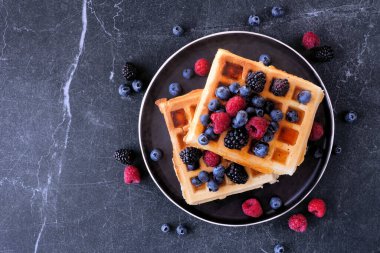 Ahududu ve yaban mersinli waffle. Koyu renkli bir arkaplan üzerinde üst görünüm.