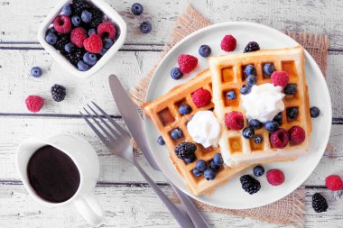 Kahvaltıda böğürtlenli waffle ve krema. Koyu taştan bir arka planda yukarıdaki masa manzarası.