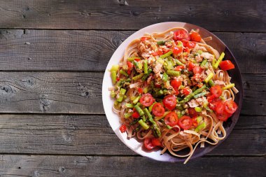 Ton balıklı makarna, taze domates ve kuşkonmaz. Koyu ahşap arka planda üst görünüm.