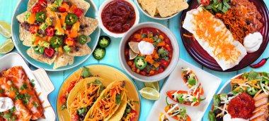 Meksika yemek masası sahnesi. Mavi ahşap arka planda manzaranın üstünde. Taco, burrito tabağı, nachos, enchilada, tortilla çorbası ve salata. Boşluğu kopyala.