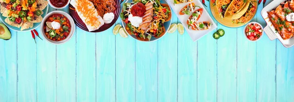 Mexican food top border. Overhead view on a blue wood banner background. Tacos, burrito plate, nachos, enchiladas, tortilla soup and salad. Copy space.