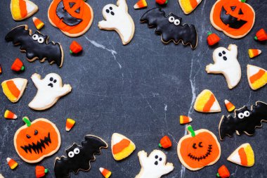 Cadılar Bayramı kurabiye çerçevesi. Fotokopi alanı olan koyu taştan bir arkaplanda üstten görünüm. Hayaletler, yarasalar, fenerler ve mısır şekeri..