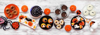 Beyaz ahşap bir arka planda ürkütücü Cadılar Bayramı tatlı masası sahnesi. Yukarıdan aşağıya doğru. Kurabiye, kek, çörek ve şeker çeşitleri..