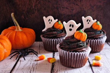 Hayaletli ve balkabaklı ürkütücü Cadılar Bayramı çikolatalı kekler. Koyu ahşap bir arka plana karşı yan görünüm masası.