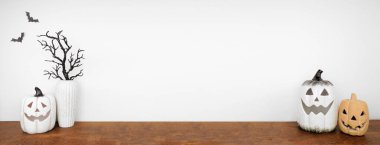 Beyaz duvar pankartıyla fotokopi çekilen Cadılar Bayramı raf dekoru. Balkabağı fenerleriyle ahşap raf ve ürkütücü dal dekorları..