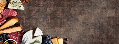 Şarküteri peyniri, et ve aperatif koleksiyonu. Üstten aşağı görünüm kenarı, fotokopi alanı olan koyu taştan bir arkaplan üzerinde.