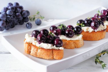 Kızarmış üzüm ve çırpılmış peynirli Crostini aperatifleri. Masa sahnesini beyaz bir arkaplanla kapatın. Parti yemeği konsepti.