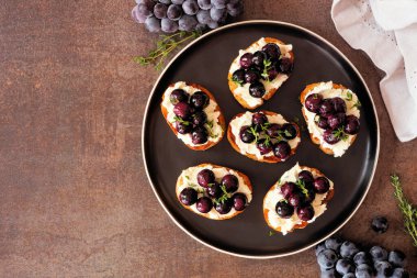 Kızarmış üzüm ve çırpılmış peynirli Crostini aperatifleri. Masanın üstünde, karanlık bir arkaplanda. Parti yemeği konsepti.