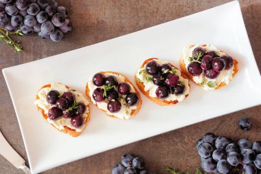 Kızarmış üzüm ve çırpılmış peynirli Crostini aperatifleri. Yukarıdan aşağıya manzara masası sahnesi ile karanlık bir arkaplan. Parti yemeği konsepti.