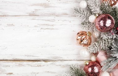 Karlı dalların, buzlu pembe kurdelelerin ve gül sarısı süslemelerin Noel kenarı. Beyaz ahşap arka planda manzaranın üstünde. Boşluğu kopyala.