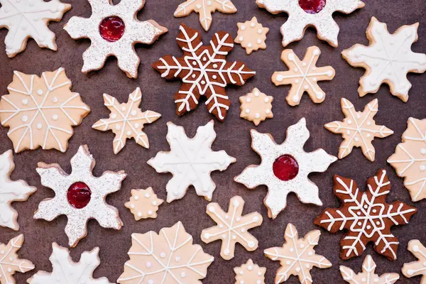 Christmas baking background with an assortment of snowflake cookies. Top down view on a dark stone background. Holiday baking concept.