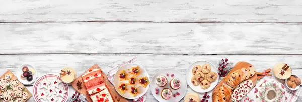 Christmas food bottom border. Top view on a white wood banner background. Assortment of appetizers and delicious sweets. Copy space. Holiday party food concept.