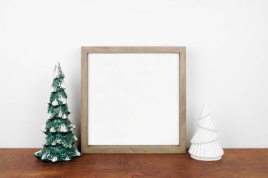 Noel, ahşap çerçeve ve ağaç süsüyle süslenir. Beyaz bir duvara karşı ahşap bir rafta kare çerçeve. Boşluğu kopyala.