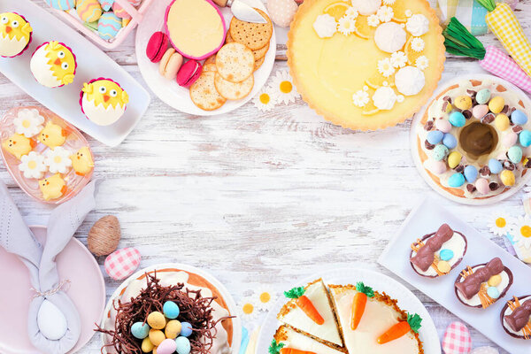Easter or spring dessert food frame. Top down view over a white wood background. Lemon tart, cupcakes, Easter egg and carrot cakes and a collection of sweets. Copy space.