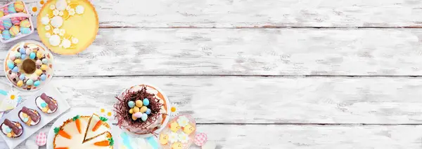 Easter or spring dessert food corner border. Overhead view on a white wood banner background. Lemon tart, cupcakes, Easter egg and carrot cakes and a selection of sweets. Copy space.