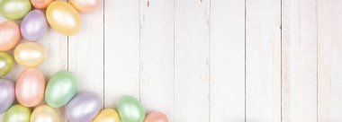 Paskalya Yumurtası sınırında beyaz ahşap bir afiş var. Parlak pastel yumurtalar. Boşluğu kopyala.