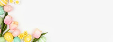 Paskalya yumurtaları ve çiçek süslemeleri. Beyaz pankartın arkasında, köşedeki sınırın üstünde. Boşluğu kopyala.