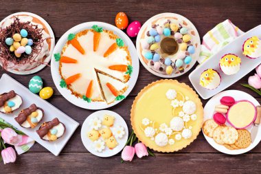 Paskalya ya da bahar tatlı masası sahnesi. Koyu renk ahşap bir arka plan. Limonlu tart, kekler, Paskalya yumurtası ve havuçlu kek ve bir sürü tatlı..