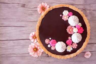 Tatlı çikolatalı tart ve pembe çikolata çiçekleri. Ahşap arka planda çiçekler olan bir masa manzarası. Bahar pişirme konsepti.