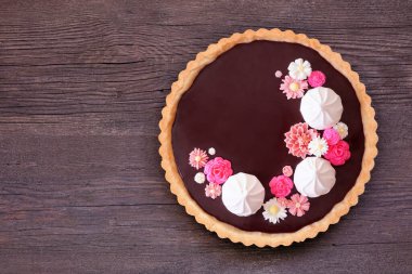 Kremalı ve pembe çikolata çiçekli lezzetli çikolatalı tart. Koyu bir ahşap arka planda, manzaranın üstünde. Bahar pişirme konsepti.