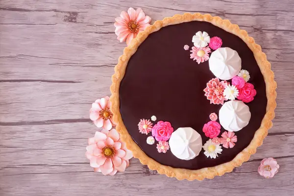 Tatlı çikolatalı tart ve pembe çikolata çiçekleri. Ahşap arka planda çiçekler olan bir masa manzarası. Bahar pişirme konsepti.