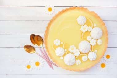 Beyaz çikolata çiçekleri ve kremalı limonlu turta. Beyaz ahşap bir arkaplan üzerinde üst görünüm tablo sahnesi.