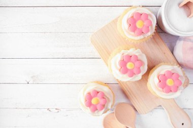 Servis tabağında pembe bahar çiçeği kekleri. Beyaz ahşap arka planlı, yukarıdan aşağıya bakan masa sahnesi. Boşluğu kopyala.