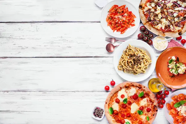 Delicious Italian food side border. Assortment of pizzas, pastas, gnocchi, risotto and bruschetta. Top down view on a white wood background. Copy space.