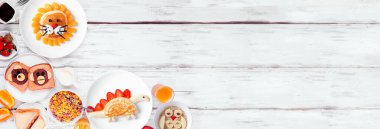 Eğlenceli çocuk temalı kahvaltı köşesi sınırında çeşitli hayvan temalı yiyecekler. Beyaz ahşap bir arkaplanda manzaranın üstünde. Gözleme, yulaf ezmesi, tost, meyve ve tahıl.