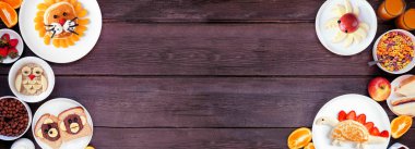 Eğlenceli çocuk temalı kahvaltı çeşitli hayvan temalı yiyeceklerle sınırlandırılmış. Koyu ahşap bir arkaplanda manzaranın üstünde. Gözleme, yulaf ezmesi, tost, meyve ve tahıl.