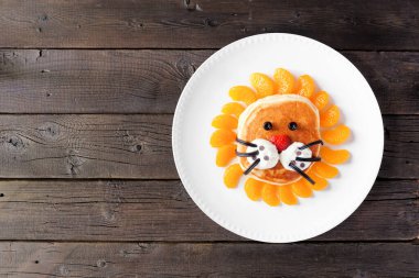 Eğlenceli çocuk temalı kahvaltı pankeki. Aslan suratlı. Koyu bir ahşap arka planda tepeden aşağı manzara.