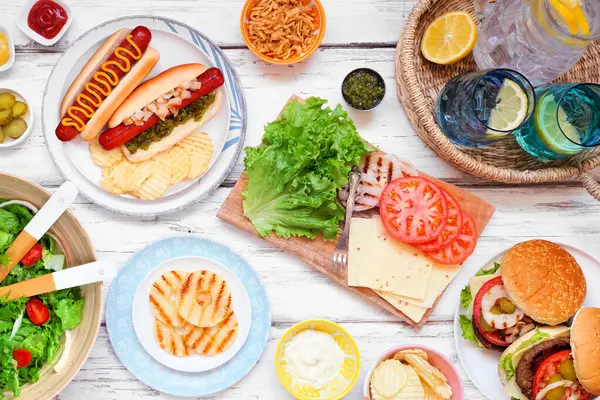 ハンバーガー ホットドッグ サラダ スナック付きの夏のBbqやピクニックテーブルシーン ホワイトウッドの背景のトップビュー ストック画像