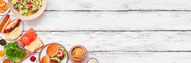 Yaz barbeküsü ya da hamburger, sosisli sandviç, salata ve abur cuburla piknik köşesi sınırı. Beyaz ahşap bir arkaplanda manzaranın üstünde. Boşluğu kopyala.