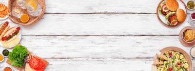 Yaz barbeküsü ya da hamburger, sosisli sandviç, salata ve abur cuburla piknik. Beyaz ahşap bir arka planda yukarıdan aşağıya doğru görünüyor. Boşluğu kopyala.