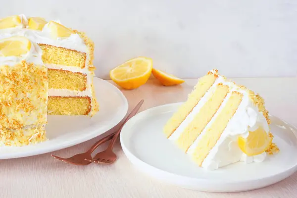 クリーミーなフロスティングで美味しいレモンケーキ 明るい背景に削除されたスライス付きのサイドビューテーブルシーン ストック画像