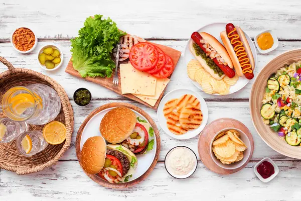 ハンバーガー ホットドッグ サラダ スナック付きの夏のBbqやピクニックテーブルシーン 白い木の背景の上下のビュー ストックフォト