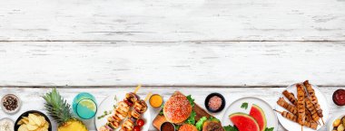Yaz BBQ gıda alt sınırı. Hamburgerler, et şişleri, patatesler, meyve ve atıştırmalıklar. Beyaz ahşap arka planda üst manzara. Boşluğu kopyala.