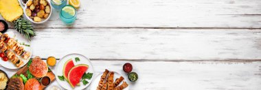 Yaz BBQ gıda köşe sınırı. Hamburgerler, et şişleri, patatesler, meyve ve atıştırmalıklar. Beyaz ahşap bir arka planda tepeden aşağı manzara. Boşluğu kopyala.