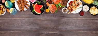 Barbekü yemekleri en üst sınırda. Hamburgerler, et şişleri, patatesler, meyve ve atıştırmalıklar. Koyu renk ahşap afiş arkaplanda yukarıdan görünüyor. Boşluğu kopyala.