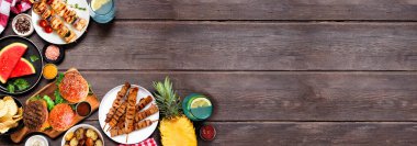 Yaz BBQ gıda köşe sınırı. Hamburgerler, et şişleri, patatesler, meyve ve atıştırmalıklar. Koyu ahşap bir arkaplanda manzaranın üstünde. Boşluğu kopyala.