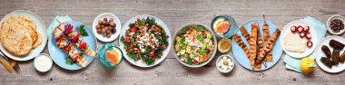 Yaz Akdeniz temalı yemek masası sahnesi. Ahşap bir arka planda genel manzara. Izgara şiş, salata, aperatif, pide ve tzatziki..