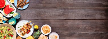 Et şişleri, salata, meyve ve abur cuburlarla dolu yaz yemekleri sınırı. Koyu renk ahşap afiş arkaplanda yukarıdan görünüyor. Boşluğu kopyala.