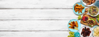 Yaz barbeküsü ya da piknik yemekleri sınırında. Hamburger, ızgara et, patates, füme mısır, meyve, salata ve aperatif. Beyaz ahşap bir arka planda tepeden aşağı manzara. Boşluğu kopyala.