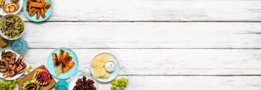 Yaz BBQ 'su ya da piknik yemekleri köşesi sınırı. Hamburger, ızgara et, patates, füme mısır, meyve, salata ve aperatif. Beyaz ahşap bir arkaplanda manzaranın üstünde. Boşluğu kopyala.