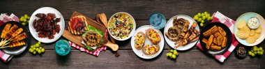 Yaz barbeküsü ya da piknik masası sahnesi. Hamburger, ızgara et, patates, mısır, meyve, salata ve aperatif. Koyu ahşap bir arkaplanda üstten görünüm.