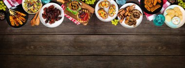 Yaz barbeküsü ya da piknik yemekleri. Hamburger, ızgara et, patates, mısır, meyve, salata ve aperatif. Koyu renk ahşap afiş arkaplanda yukarıdan görünüyor. Boşluğu kopyala.